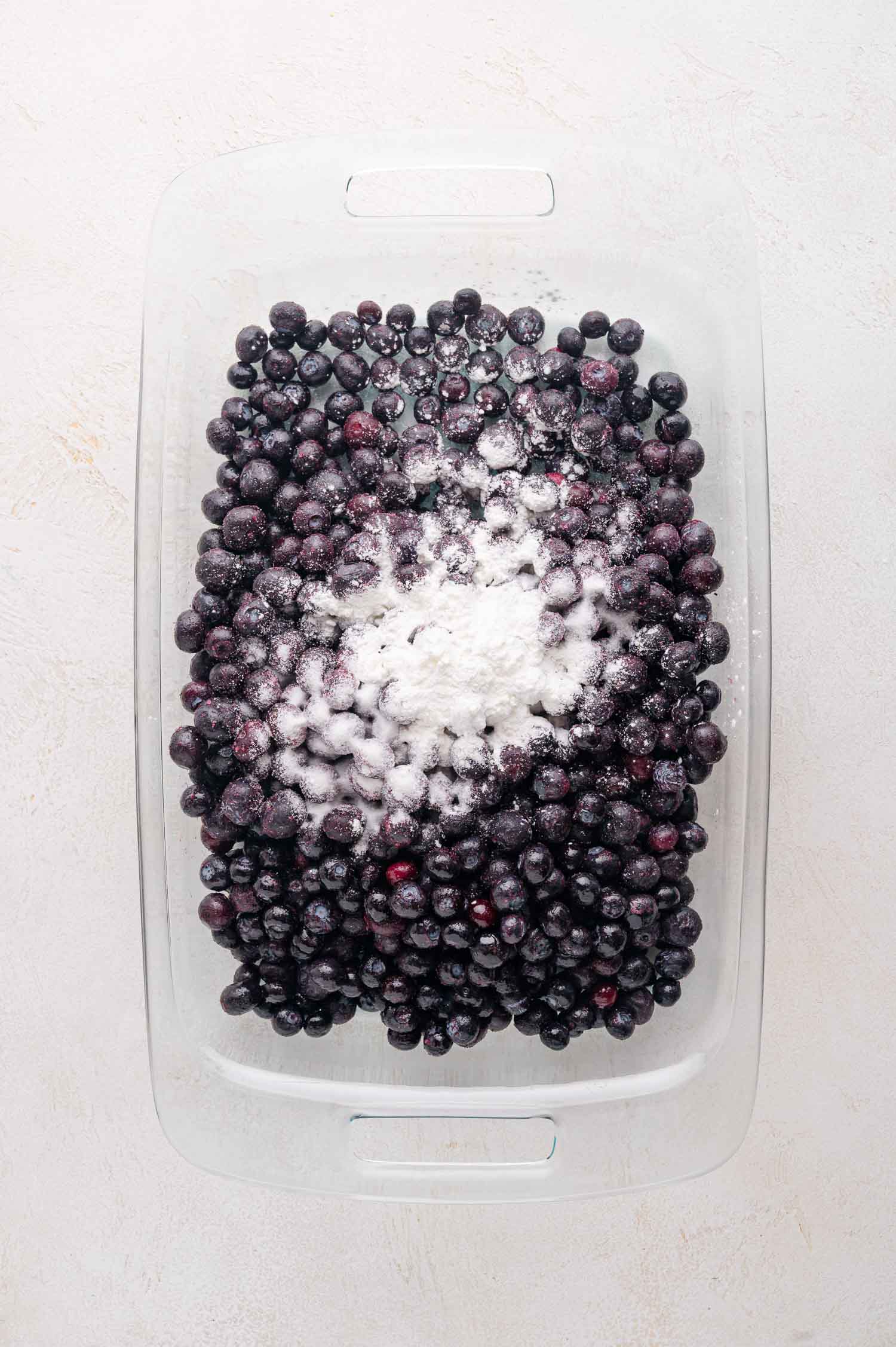 Blueberry Crumble 5 A glass baking dish filled with blueberries topped with a mound of cornstarch and sugar.