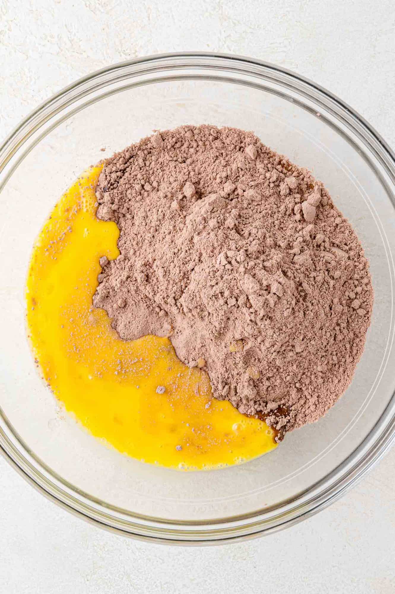 A glass bowl containing beaten eggs and dry chocolate cake mix, ready to be combined.
