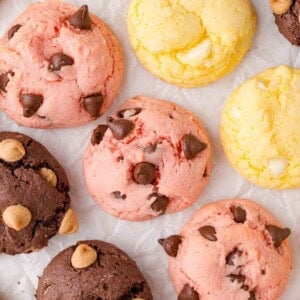 Assorted colorful cake mix cookies with chocolate chips and other toppings arranged on white parchment paper.