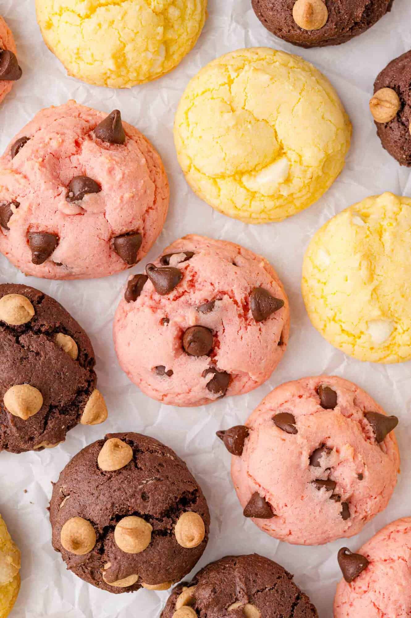 Assorted colorful cake mix cookies with chocolate chips and other toppings arranged on white parchment paper.