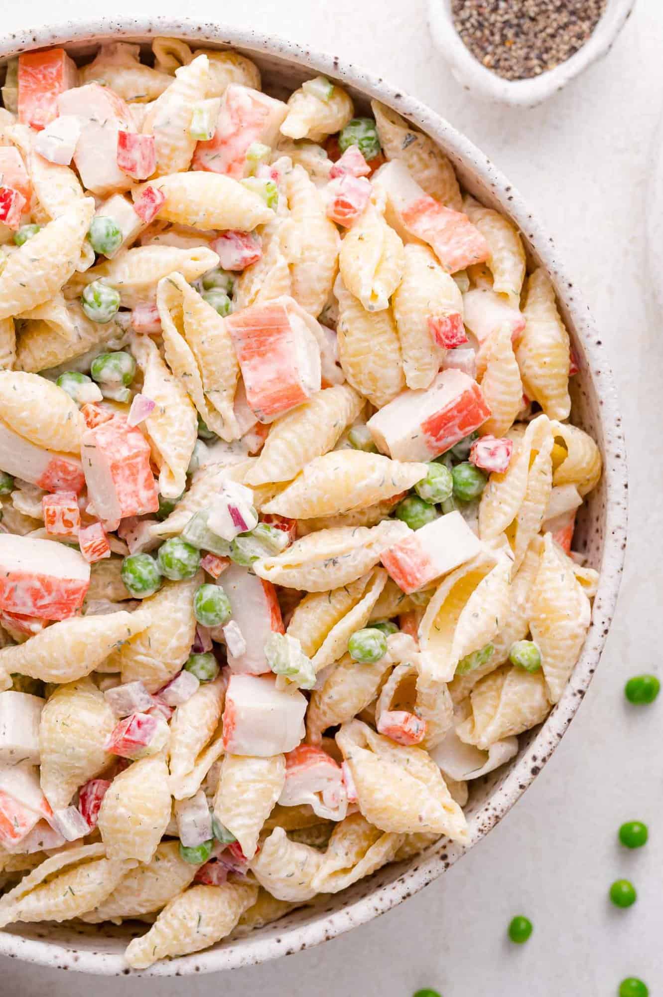 A bowl of pasta shell salad with green peas, diced imitation crab, and a creamy dressing.