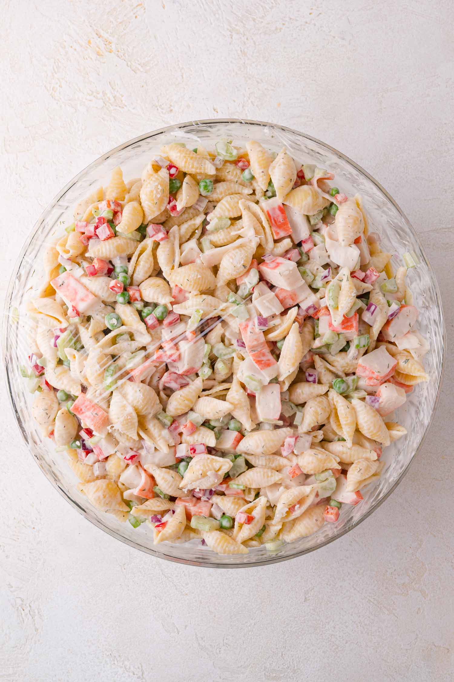 Crab Pasta Salad 13 A glass bowl filled with shell pasta salad mixed with imitation crab, chopped vegetables, and a creamy dressing, viewed from above.