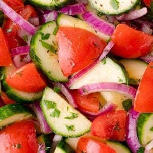 Close-up of a fresh salad with sliced cucumbers, tomatoes, red onions, and chopped herbs.