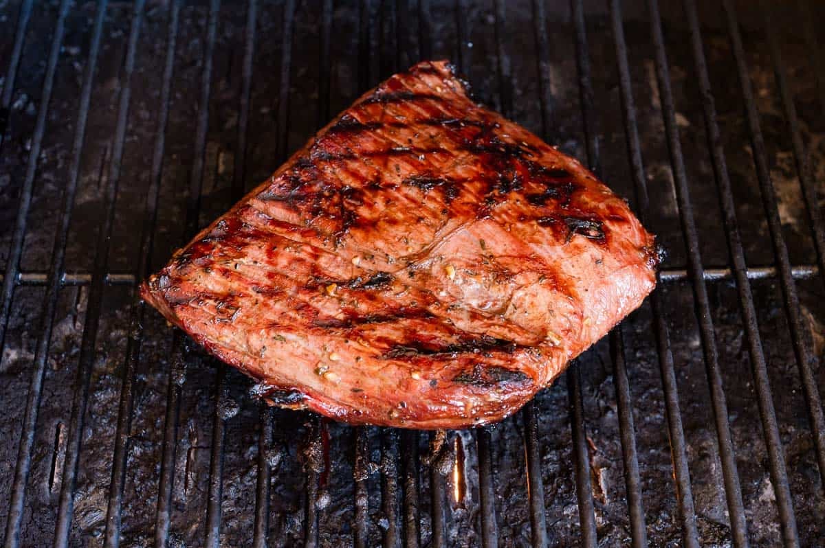 A grilled steak with grill marks sits on a metal barbecue grate.