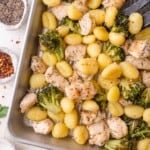 A baking tray filled with cooked gnocchi, broccoli florets, and seasoned chicken pieces.