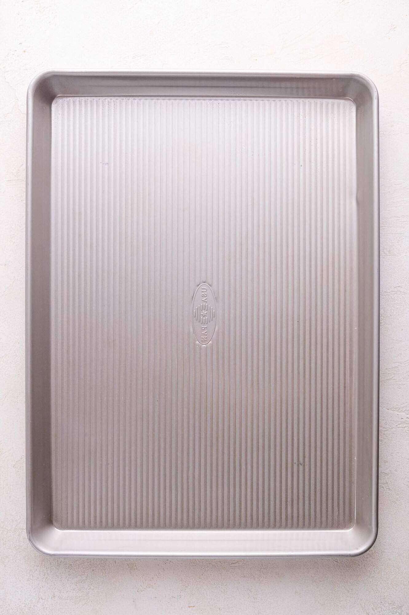 A rectangular metal sheet pan with raised edges and a textured, ridged surface, placed on a light-colored background.