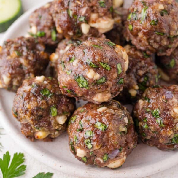 A plate of cooked meatballs mixed with chopped spinach, herbs, and cheese, arranged closely together on a white dish.