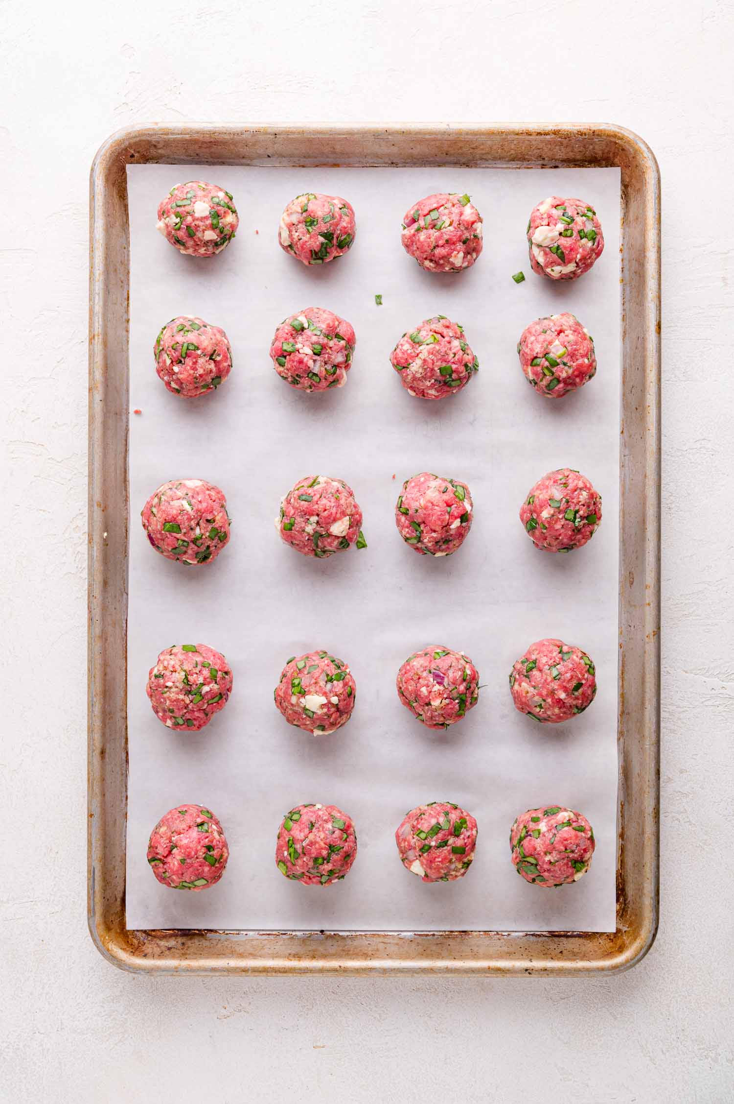 Uncooked meatballs are arranged in rows on a parchment-lined baking sheet.