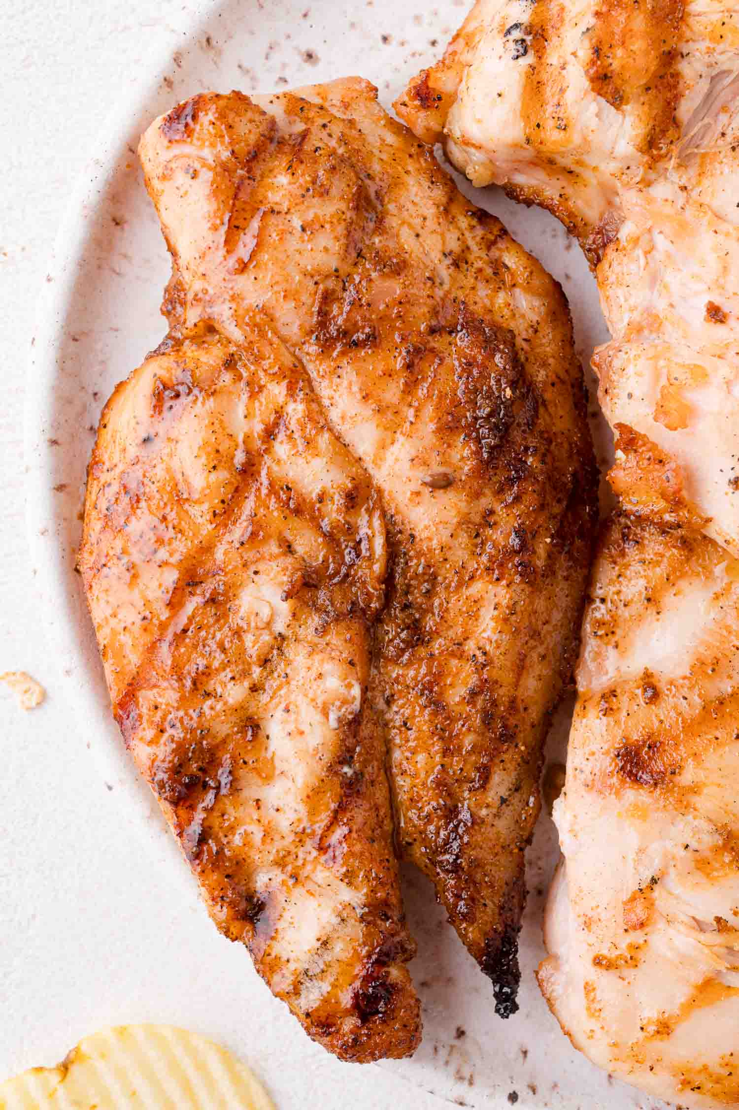 Close-up of cooked, seasoned chicken breast on a white plate.