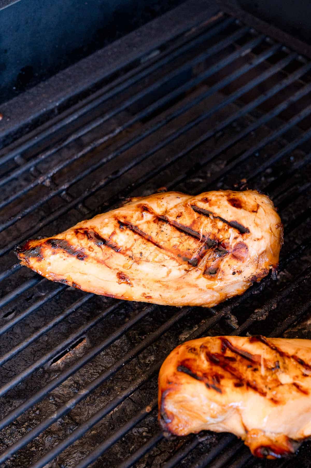 Two pieces of grilled chicken breast with visible grill marks cooking on a barbecue grill.