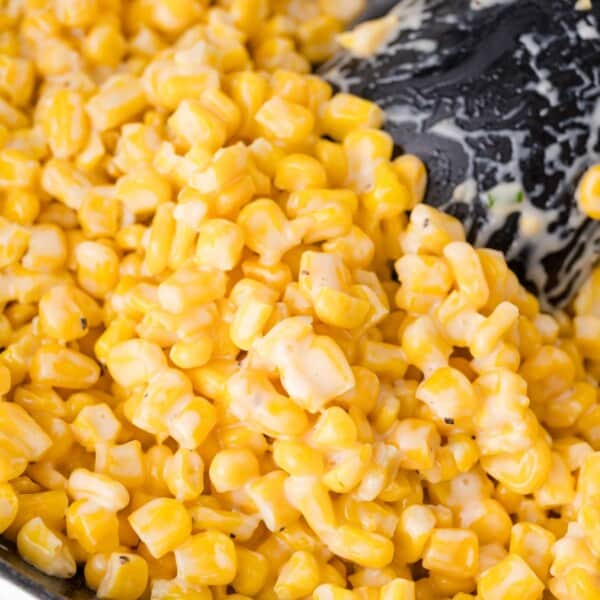Close-up of creamy corn kernels being stirred with a black utensil.