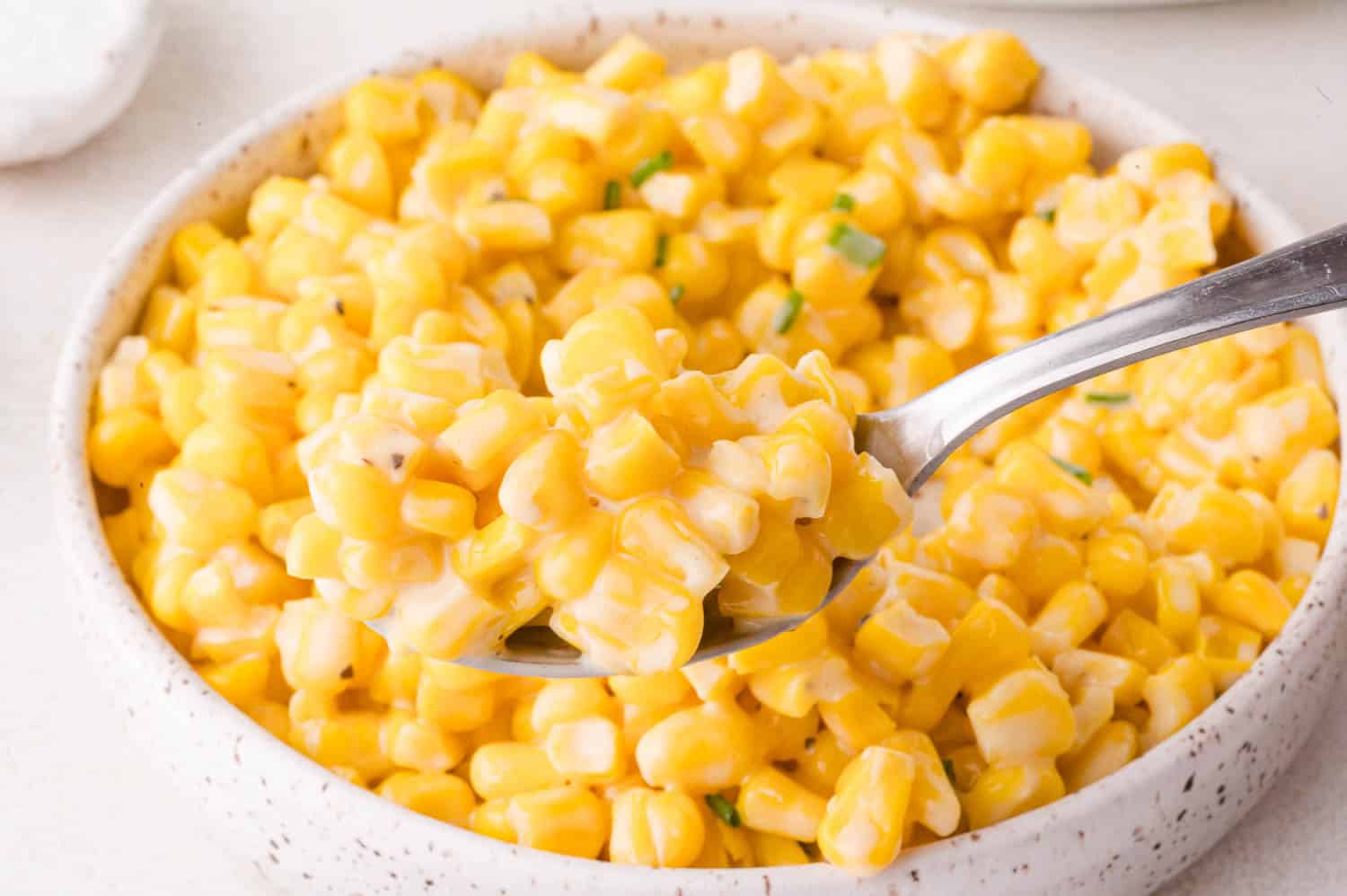 A close-up of a spoonful of creamy honey butter corn being lifted from a bowl filled with creamed corn.