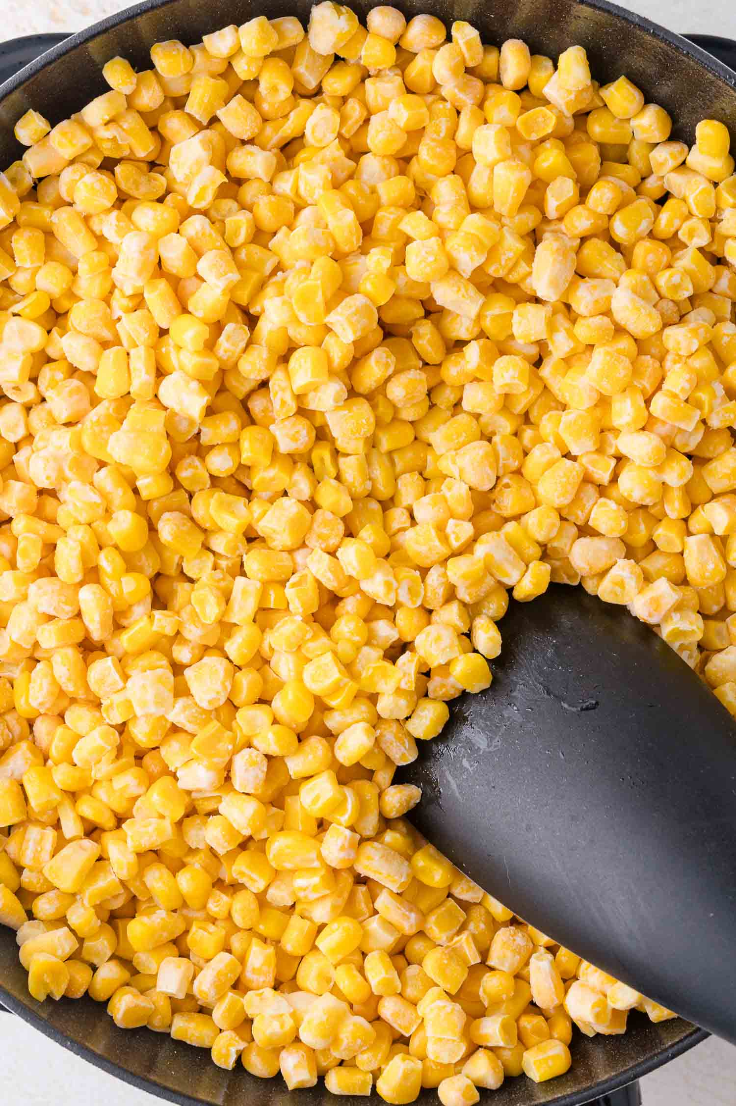 A close-up of cooked corn kernels in a pan with a black spatula.