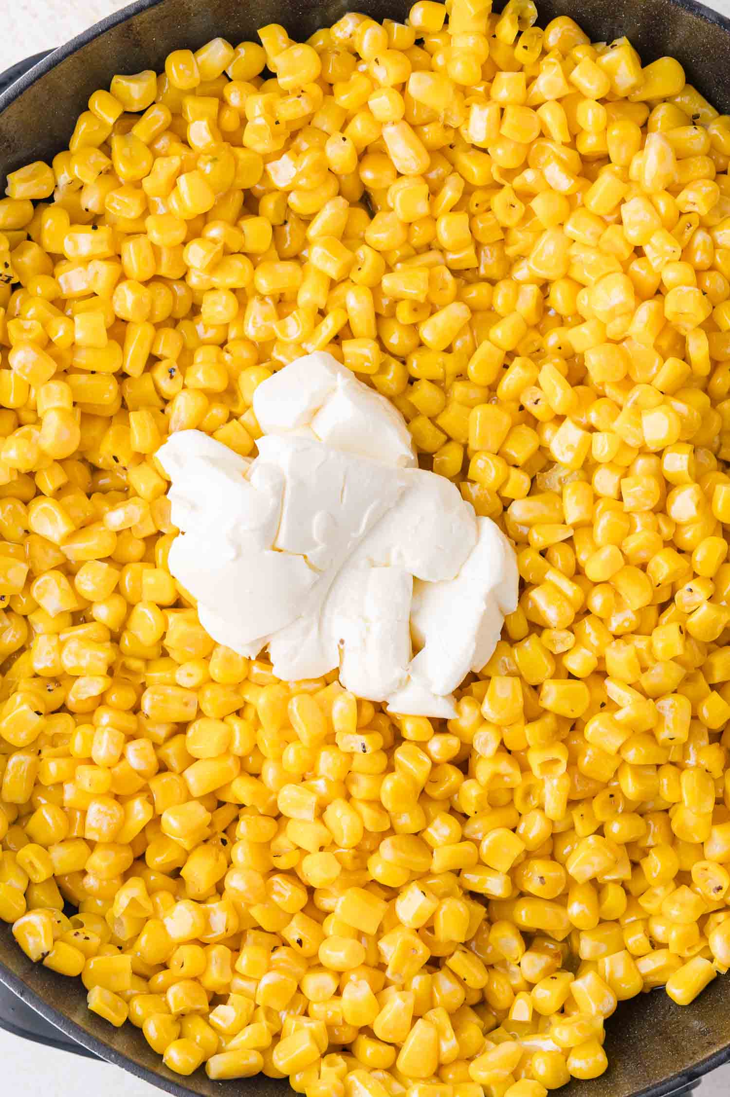 Corn kernels in a pan with a dollop of cream cheese on top.