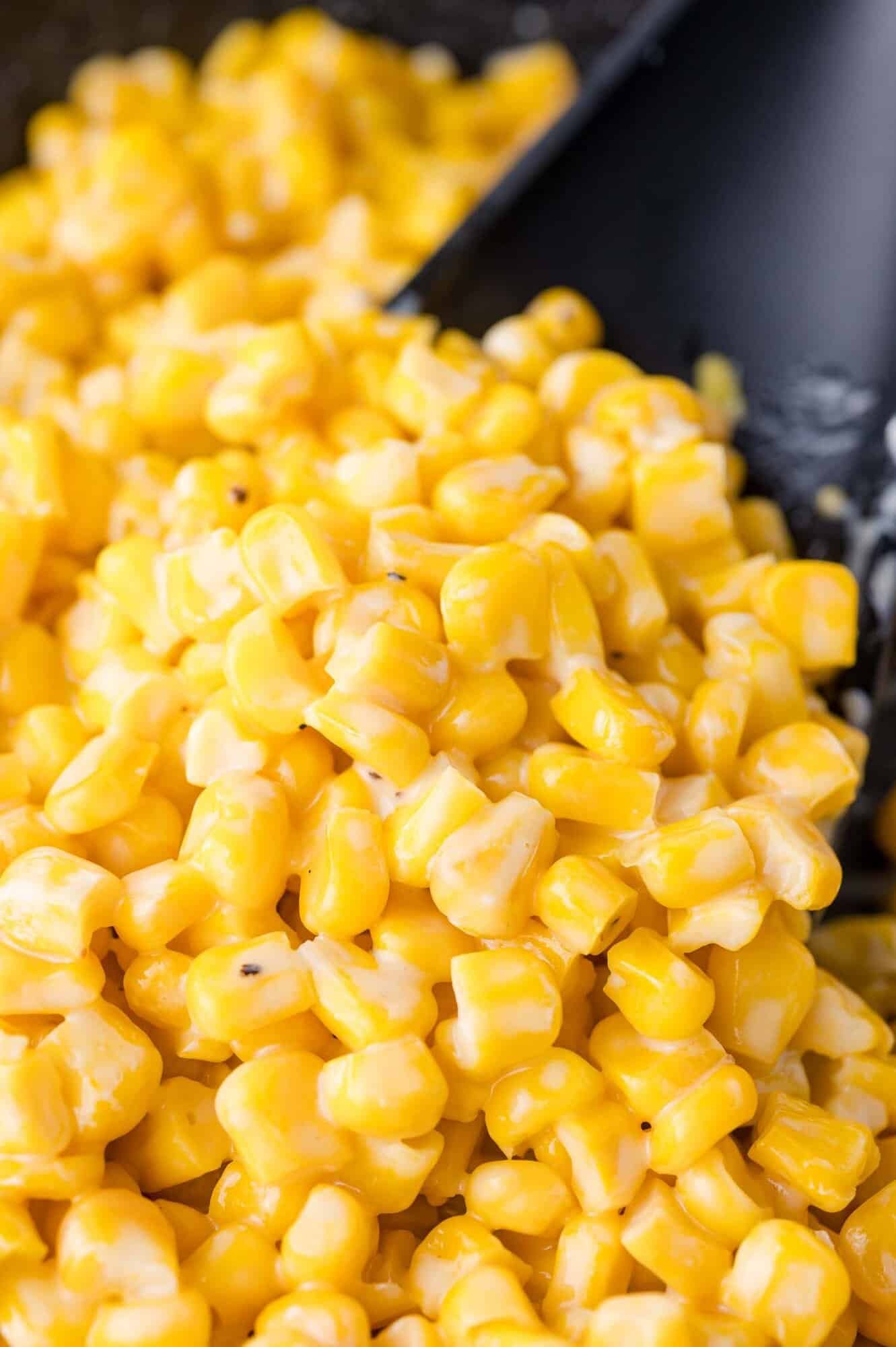 Close-up of creamy cooked corn kernels with a glossy texture, served in a black dish.