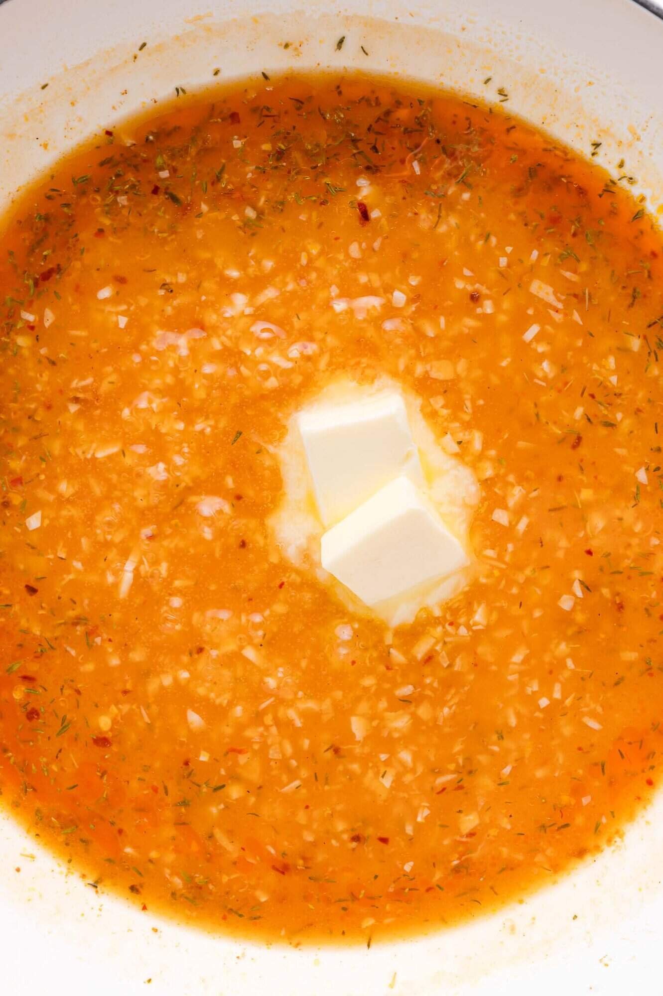 Diced garlic and spices simmer in a pot with two cubes of butter melting in the center.
