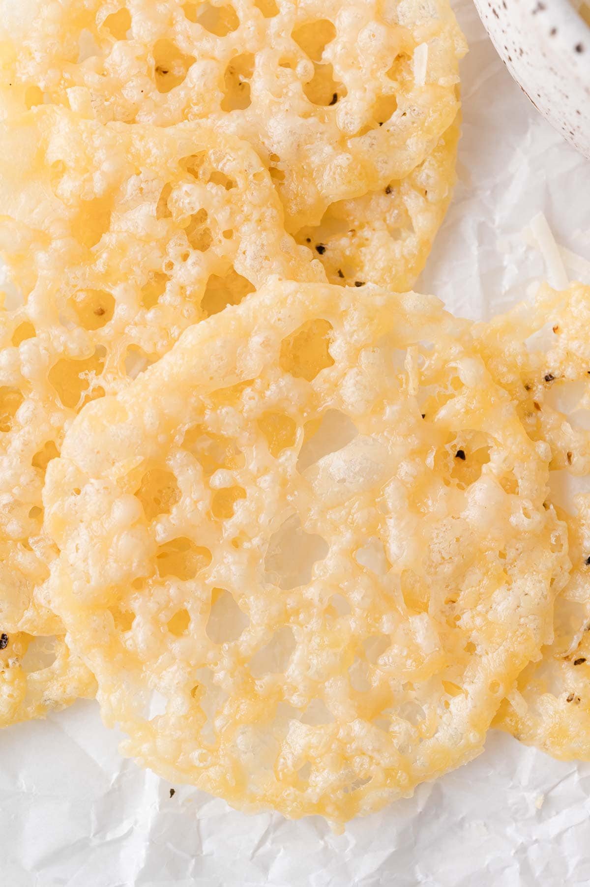 Close-up of several round, golden, lacy parmesan crisps on a sheet of white parchment paper.