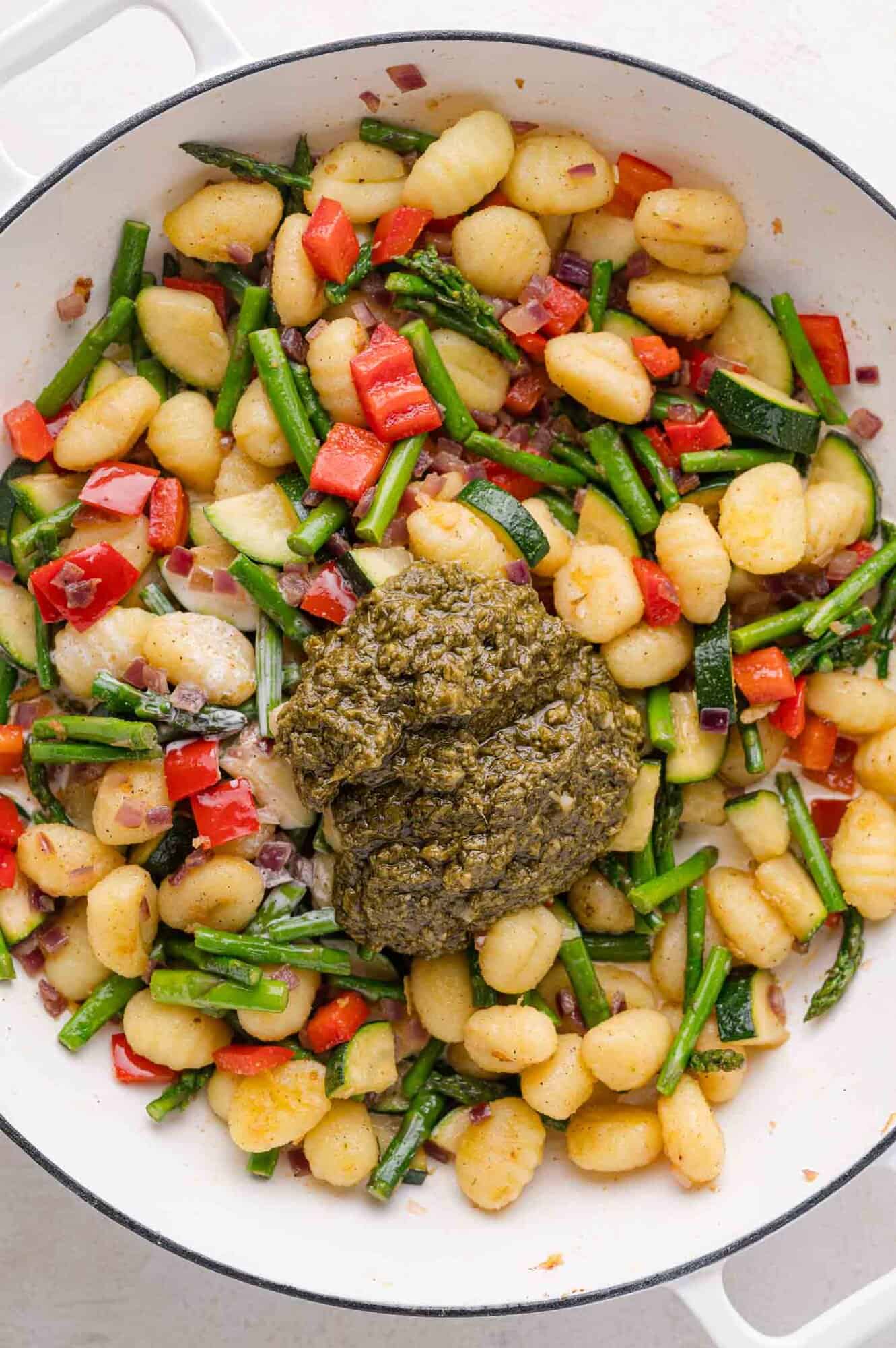 Gnocchi with chopped red bell peppers, asparagus, and zucchini in a pan, topped with a generous serving of green pesto.
