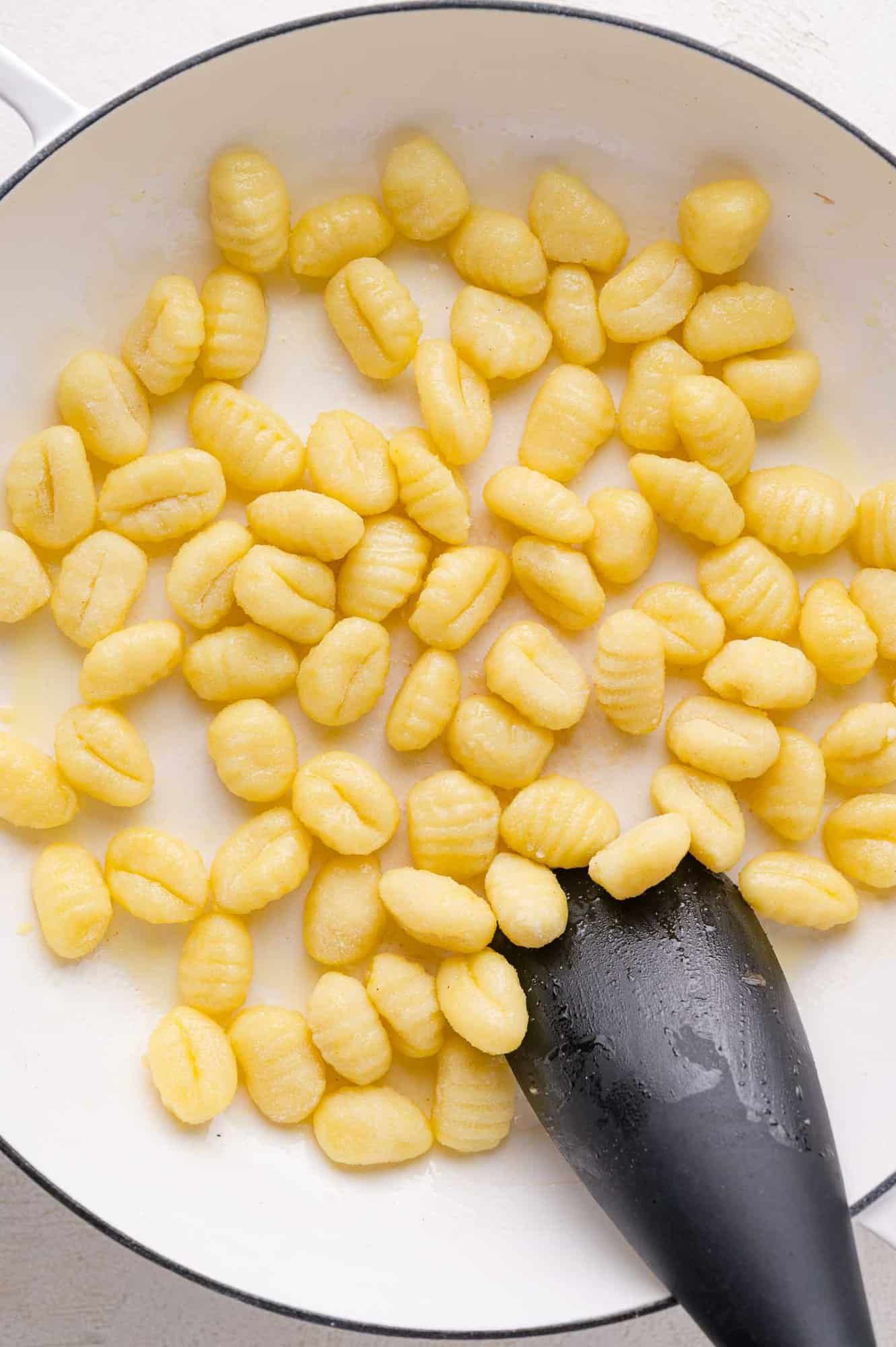 Cooked gnocchi in a white pan with a black spatula.