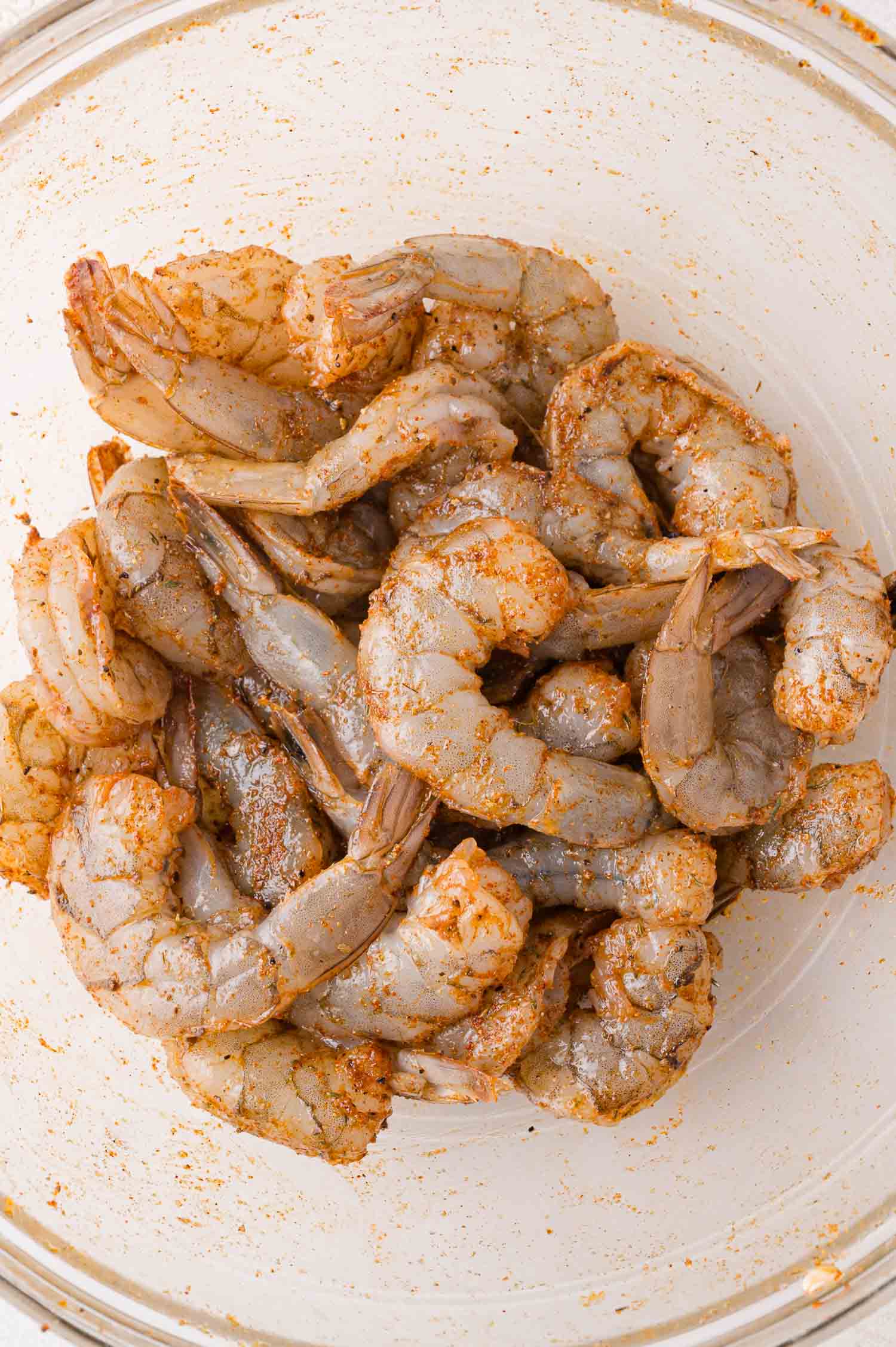 Raw shrimp coated with seasoning in a clear glass bowl.