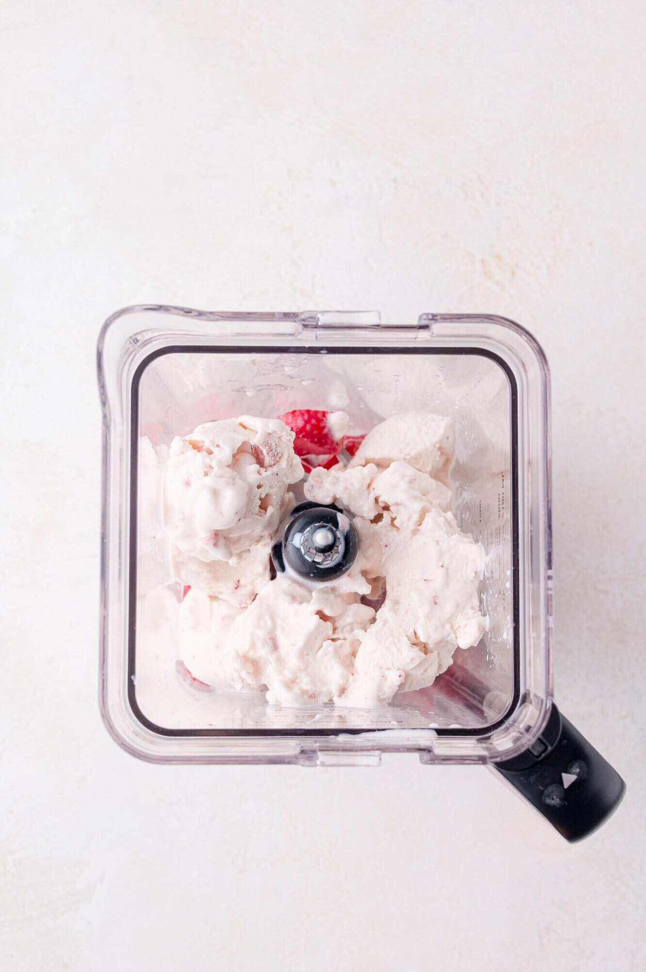A top-down view of a blender containing ice cream and strawberries on a light background.