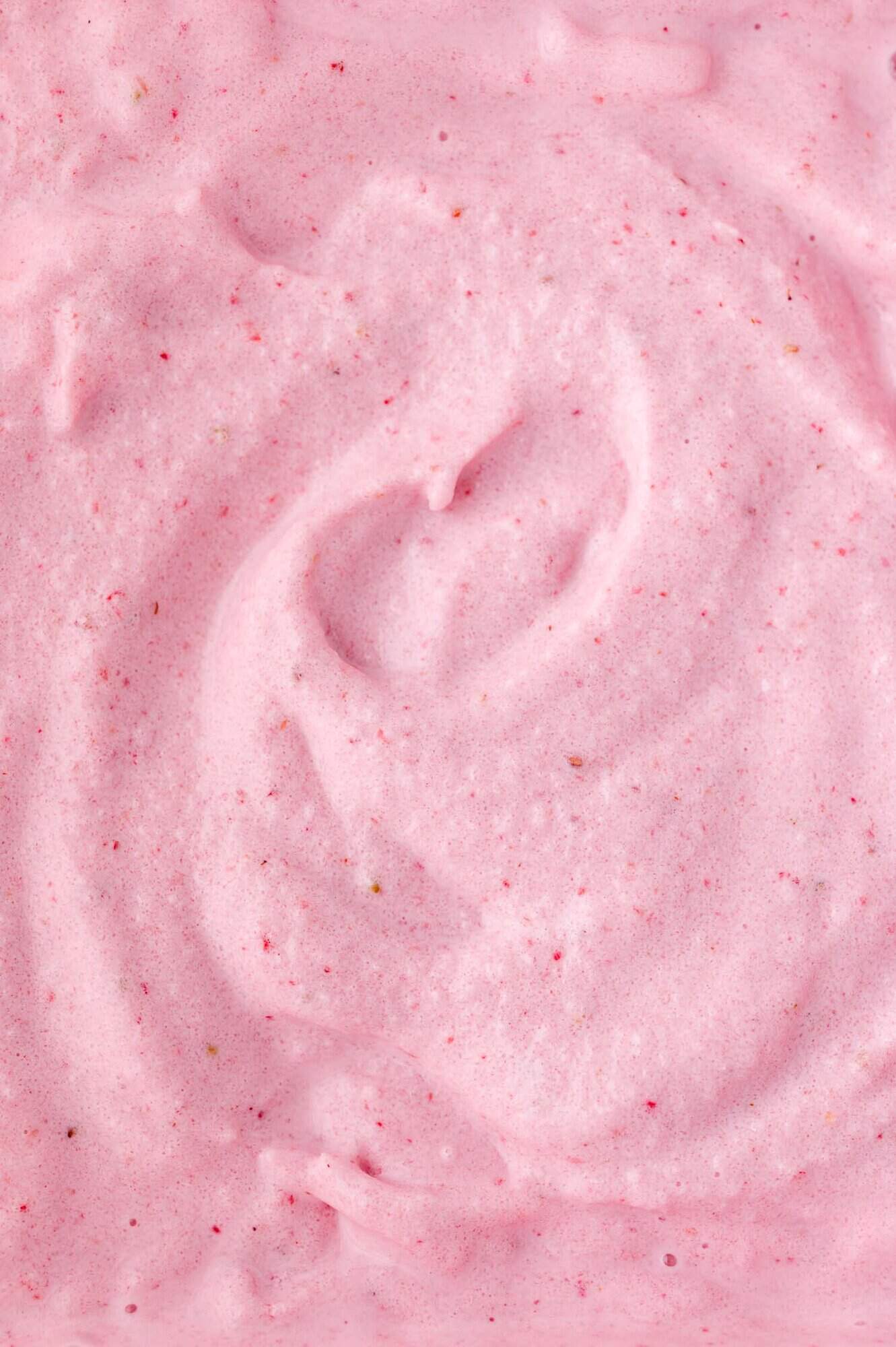 Close-up of a strawberry milkshake - pink, creamy, and slightly textured substance with small red specks.
