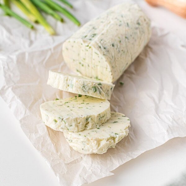 Sliced chive butter log on parchment paper, with chives in the background.