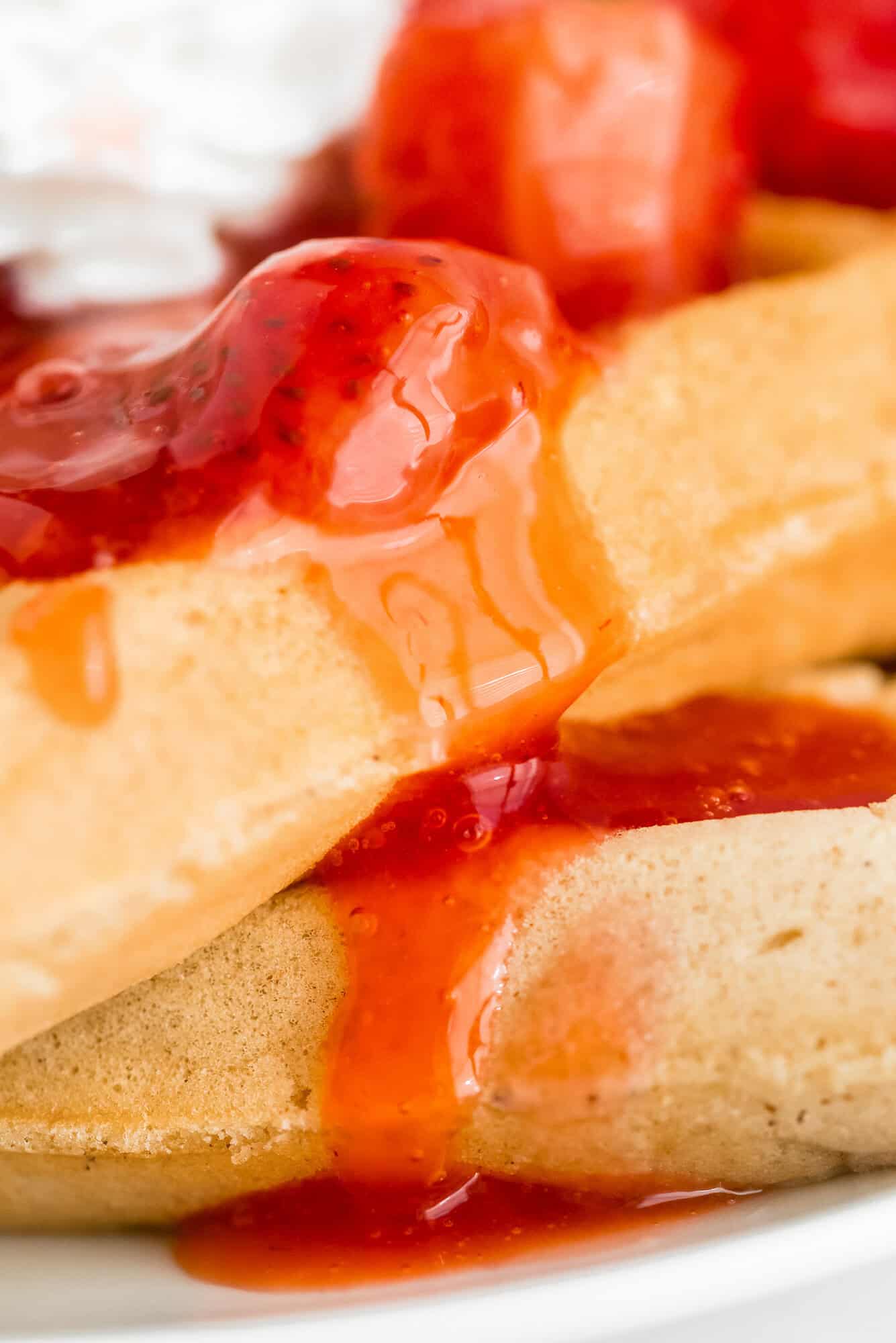 Close-up of waffles topped with strawberry sauce, with syrup dripping over the edge.