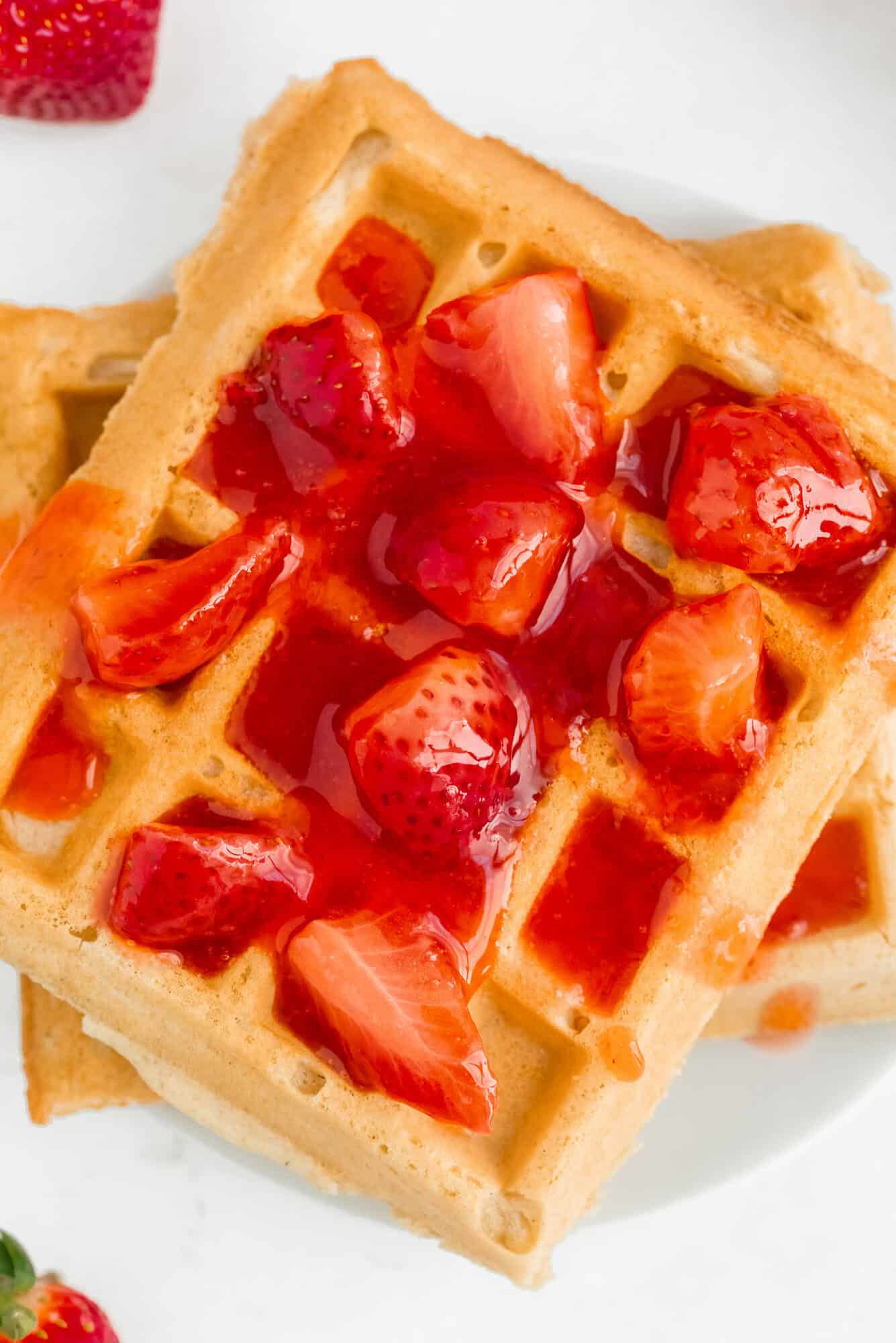 Two golden waffles topped with sliced strawberries and strawberry syrup on a white plate.