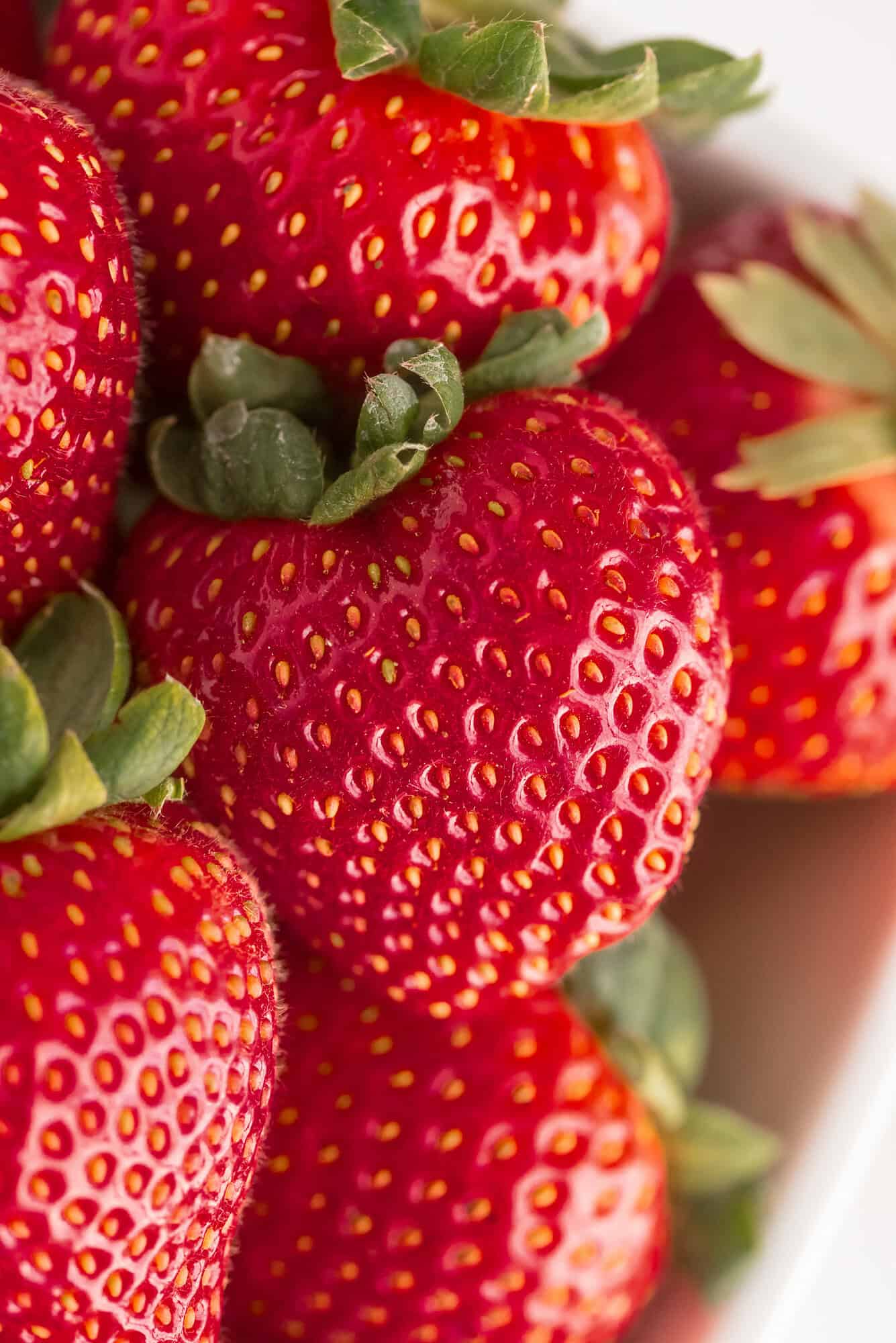 Close-up of several ripe strawberries with green leaves, showing their red skin and small yellow seeds.