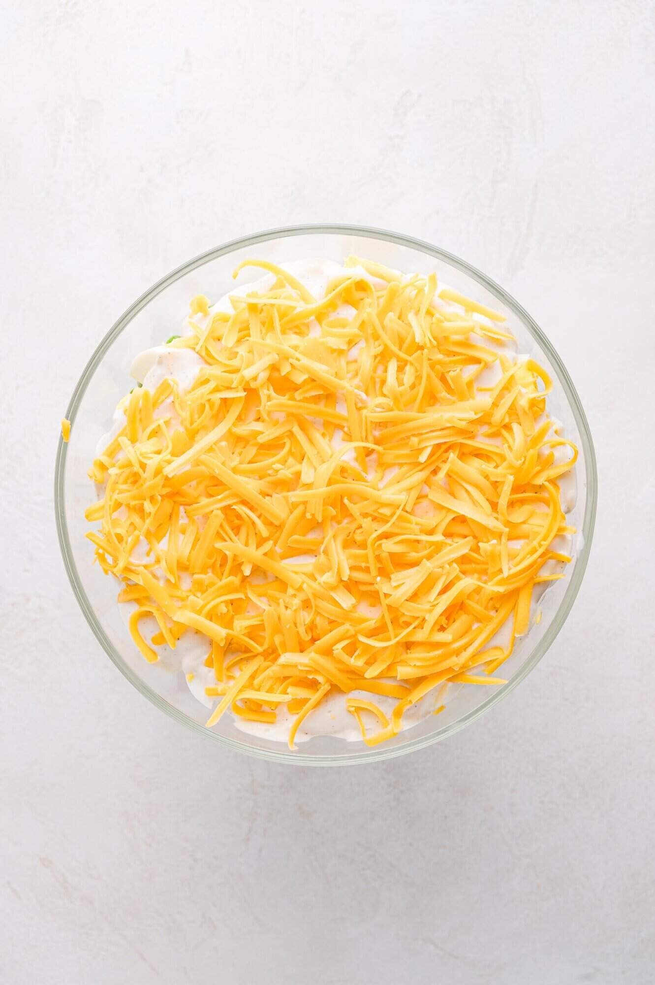 Top view of 7 layer salad topped with shredded cheddar cheese.