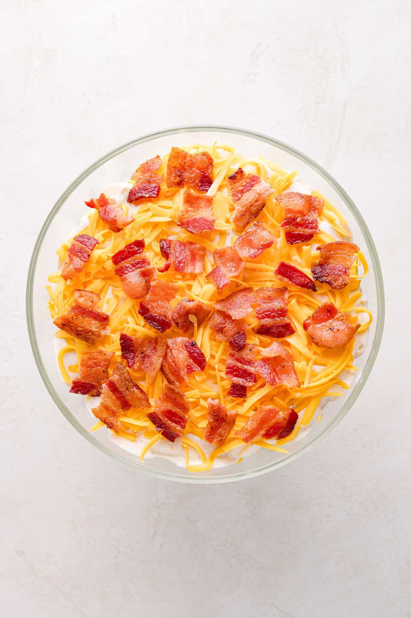 Top down view of seven layer salad with cheddar cheese and bacon visible. 