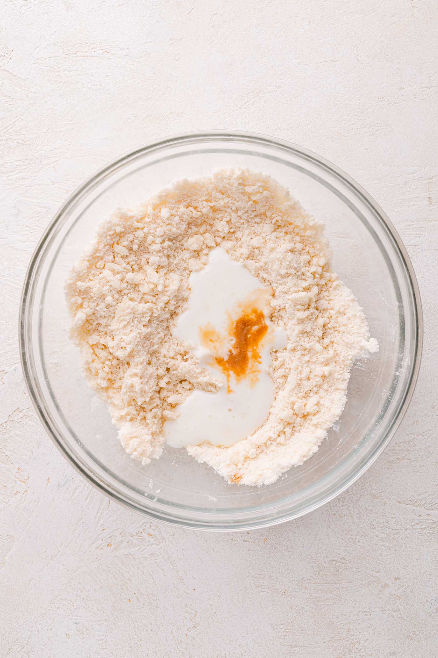 A glass bowl containing flour mixture with buttermilk and vanilla extract in the center, ready to be mixed.