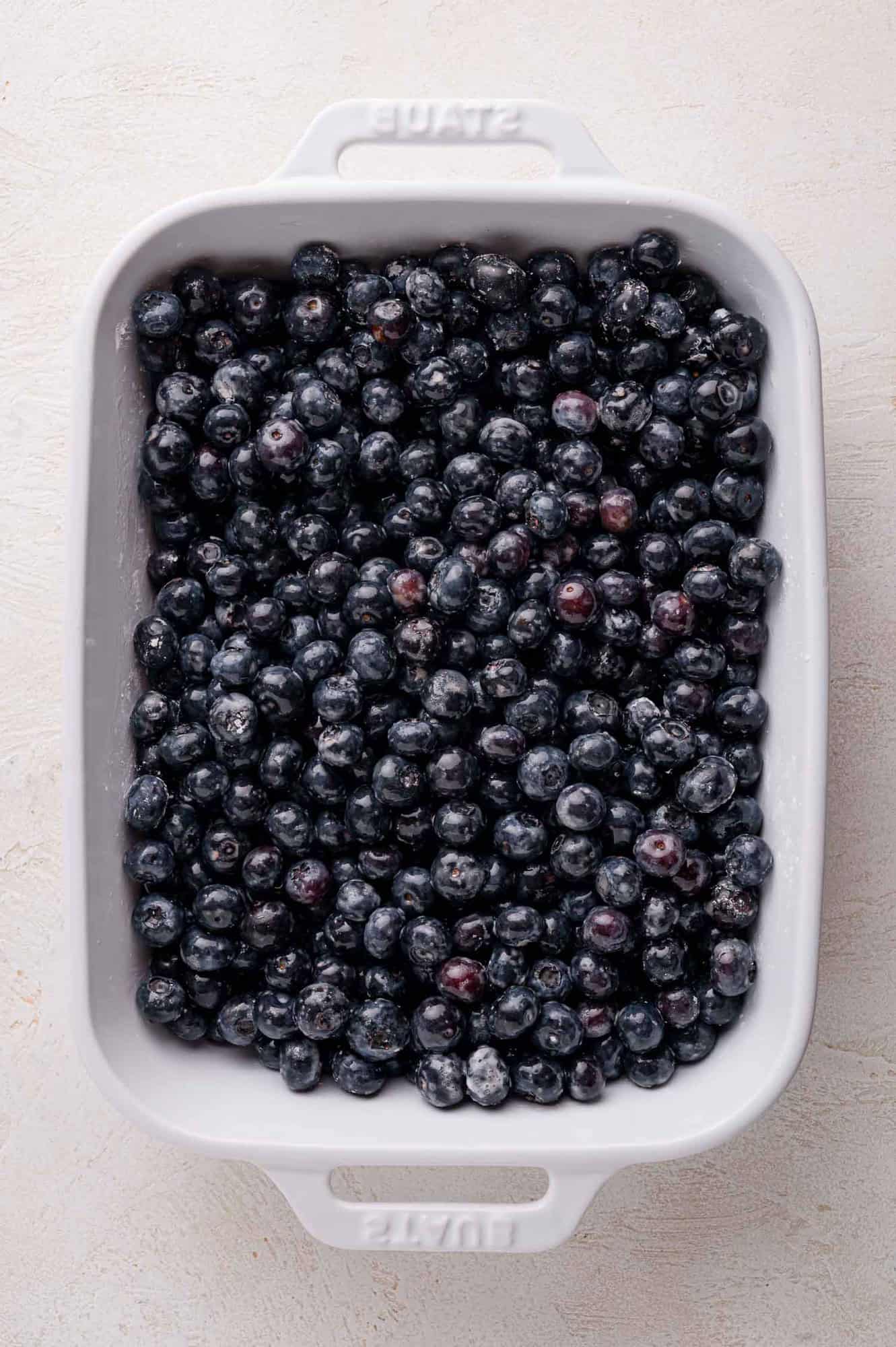 A white rectangular baking dish filled with fresh blueberries on a light-colored surface.