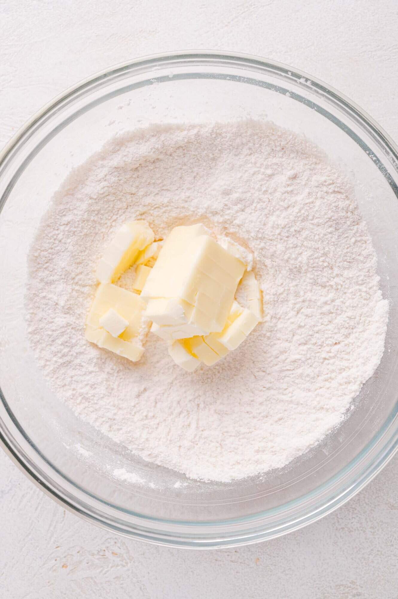 A glass bowl containing flour with cubes of butter placed on top, viewed from above.