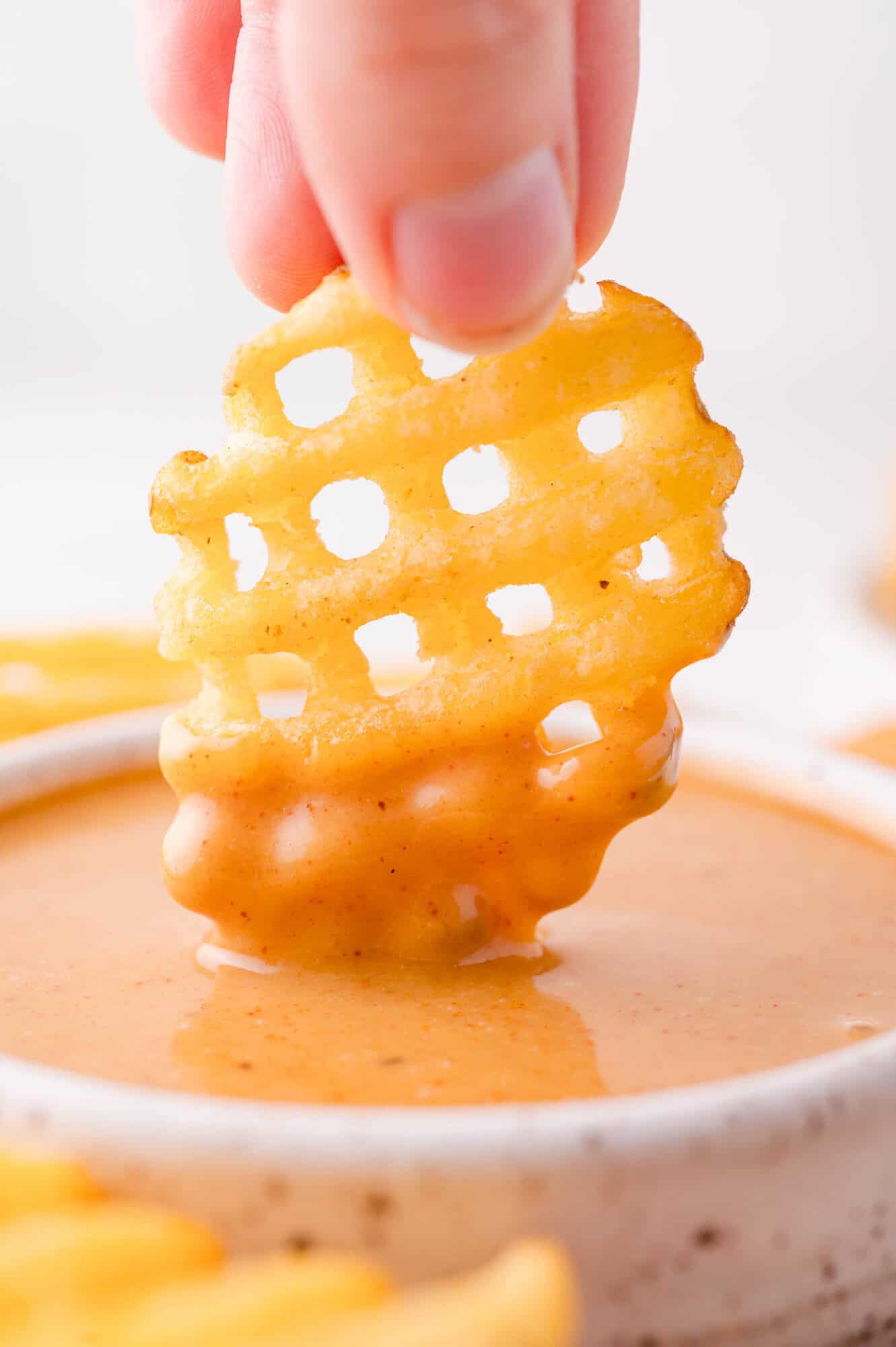 Chick-fil-A Sauce 4 A hand dips a waffle-cut French fry into a bowl of creamy, orange-colored Chick-fil-A dipping sauce.