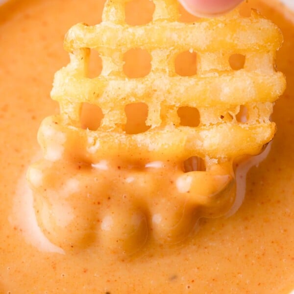 A waffle-cut French fry being dipped into a creamy orange chick-fil-a sauce.