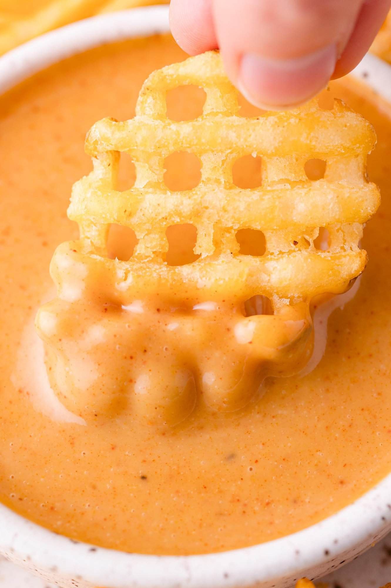 Chick-fil-A Sauce 2 A hand dips a waffle-cut french fry into a bowl of creamy orange Chick-fil-A dipping sauce.