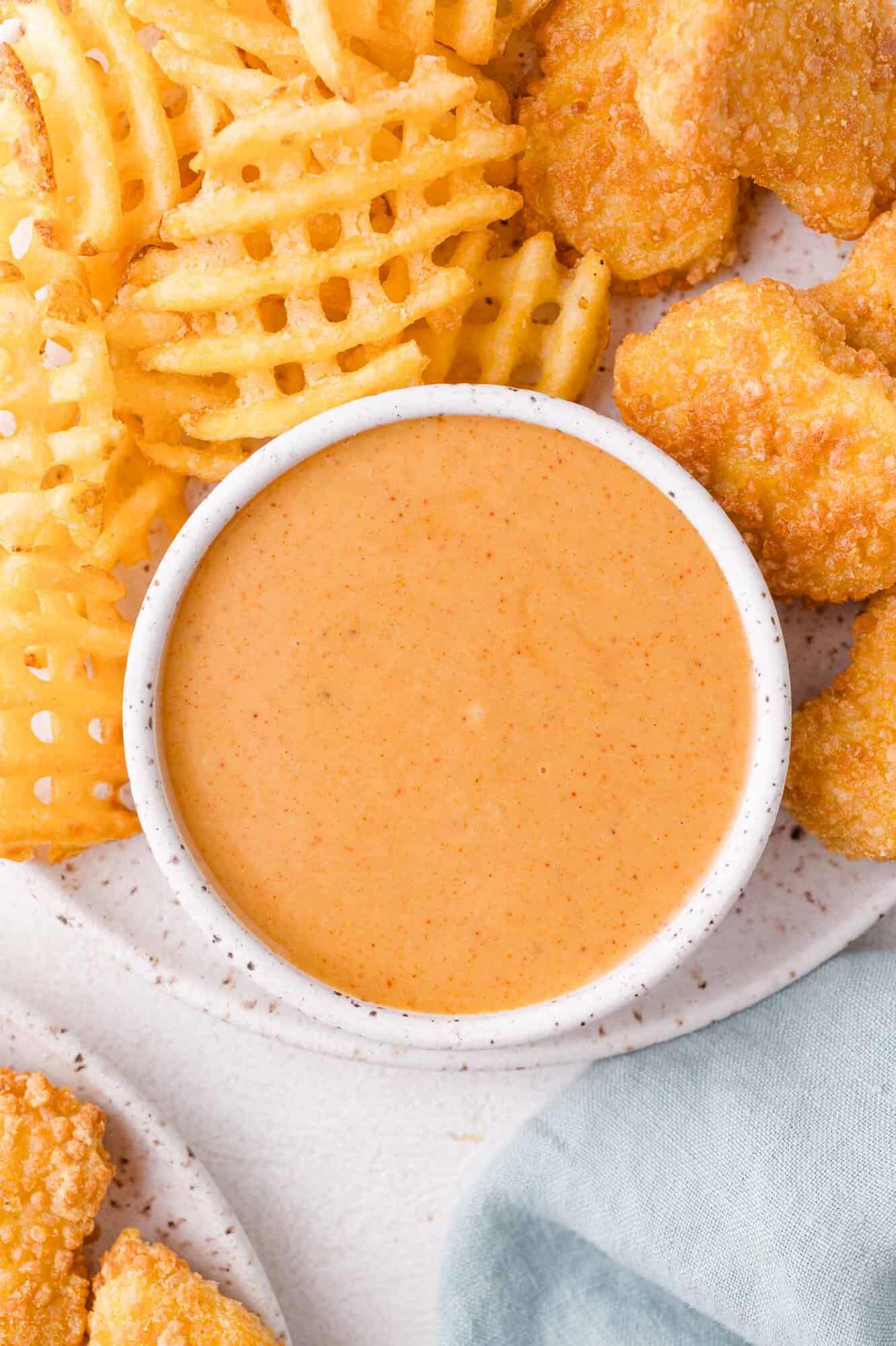 Chick-fil-A Sauce 3 A bowl of creamy dipping sauce is surrounded by waffle fries and breaded chicken nuggets on a plate.