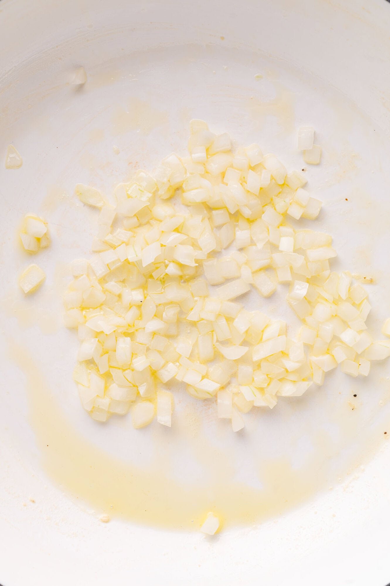 Diced onions being sautéed in oil in a white pan.