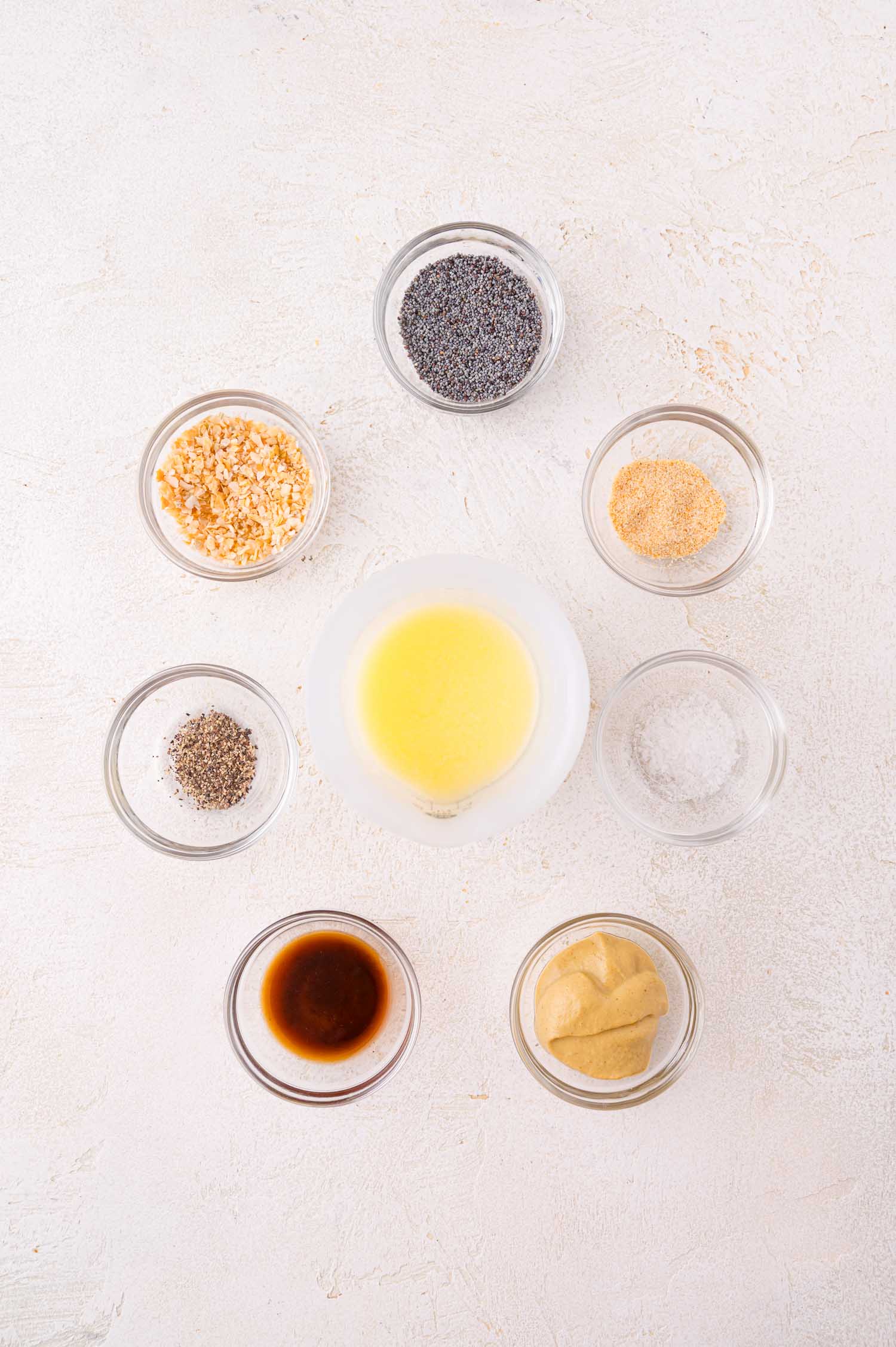 Eight small bowls containing ingredients for the topping arranged on a white surface.