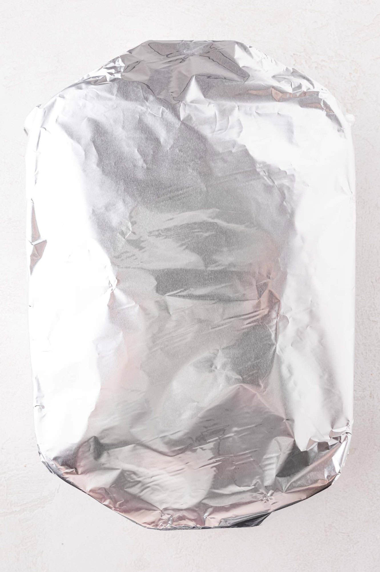 A rectangular baking dish covered with a sheet of aluminum foil, placed on a light-colored surface.