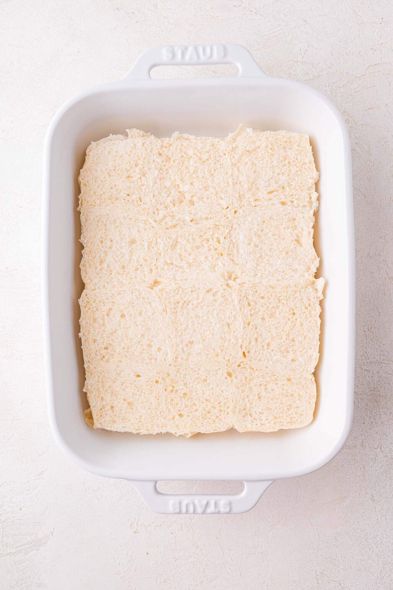 Slider roll bottom halves arranged in a single layer to cover the bottom of a white rectangular baking dish.