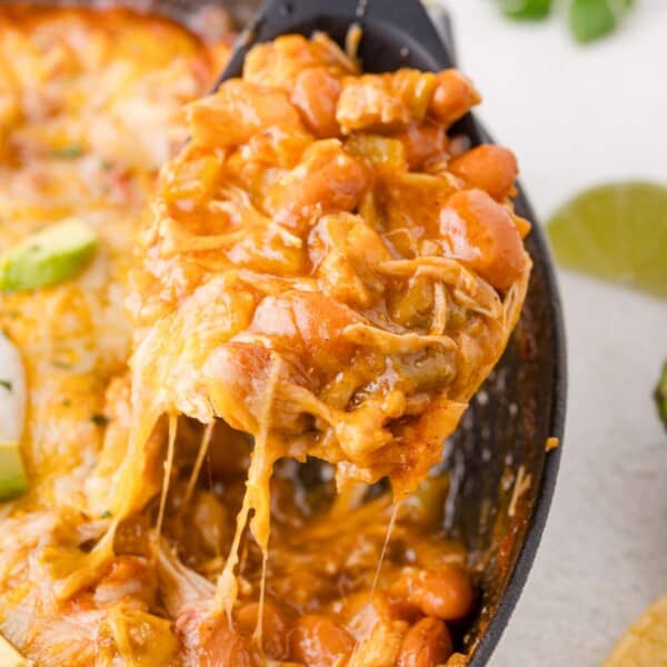 A serving of cheesy enchilada skillet being lifted from a casserole dish with a spoon, showing melted cheese stretching.