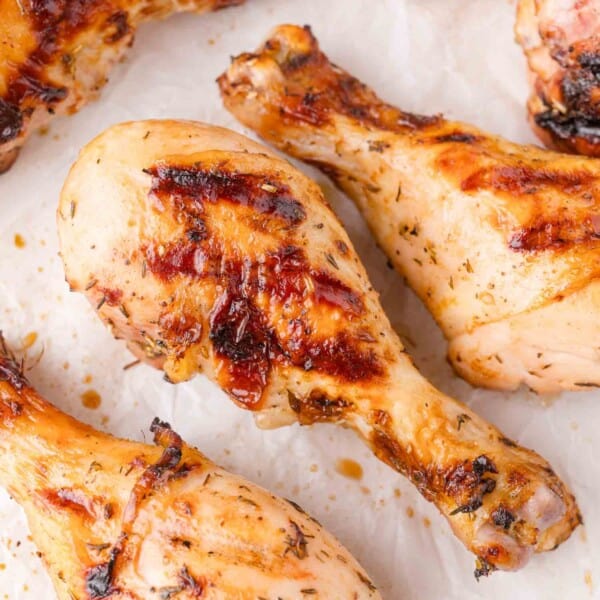 Close-up of several grilled chicken drumsticks with a golden-brown, slightly charred exterior on a sheet of parchment paper.
