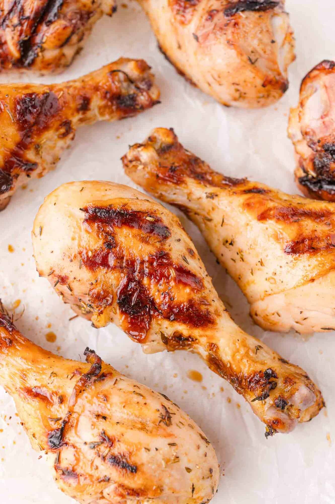 Grilled chicken drumsticks with charred grill marks, arranged on a white surface.