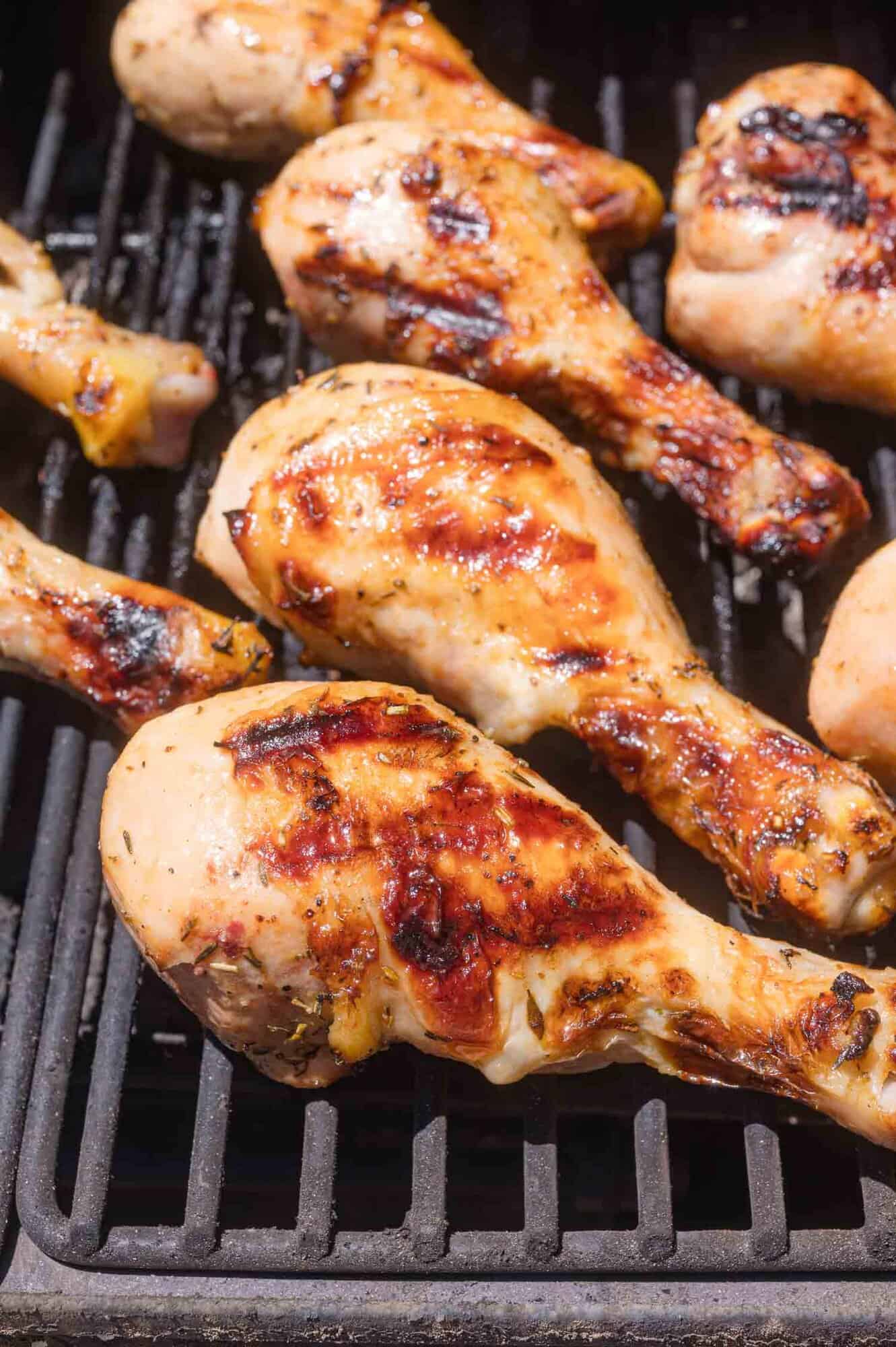 Grilled chicken drumsticks cooking on a barbecue grill, with char marks visible on the meat.