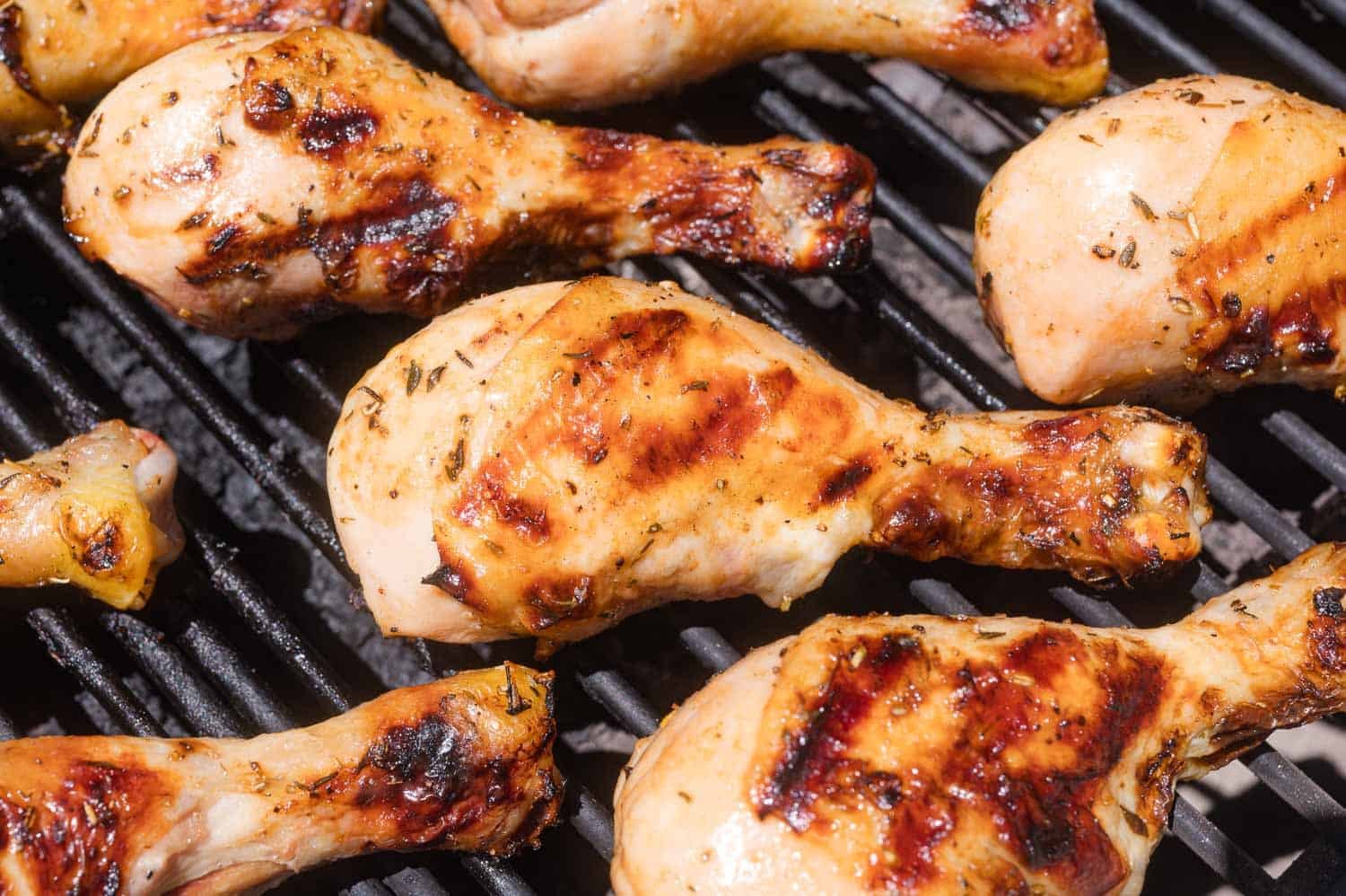 Several seasoned chicken drumsticks cooking on a grill with visible char marks.