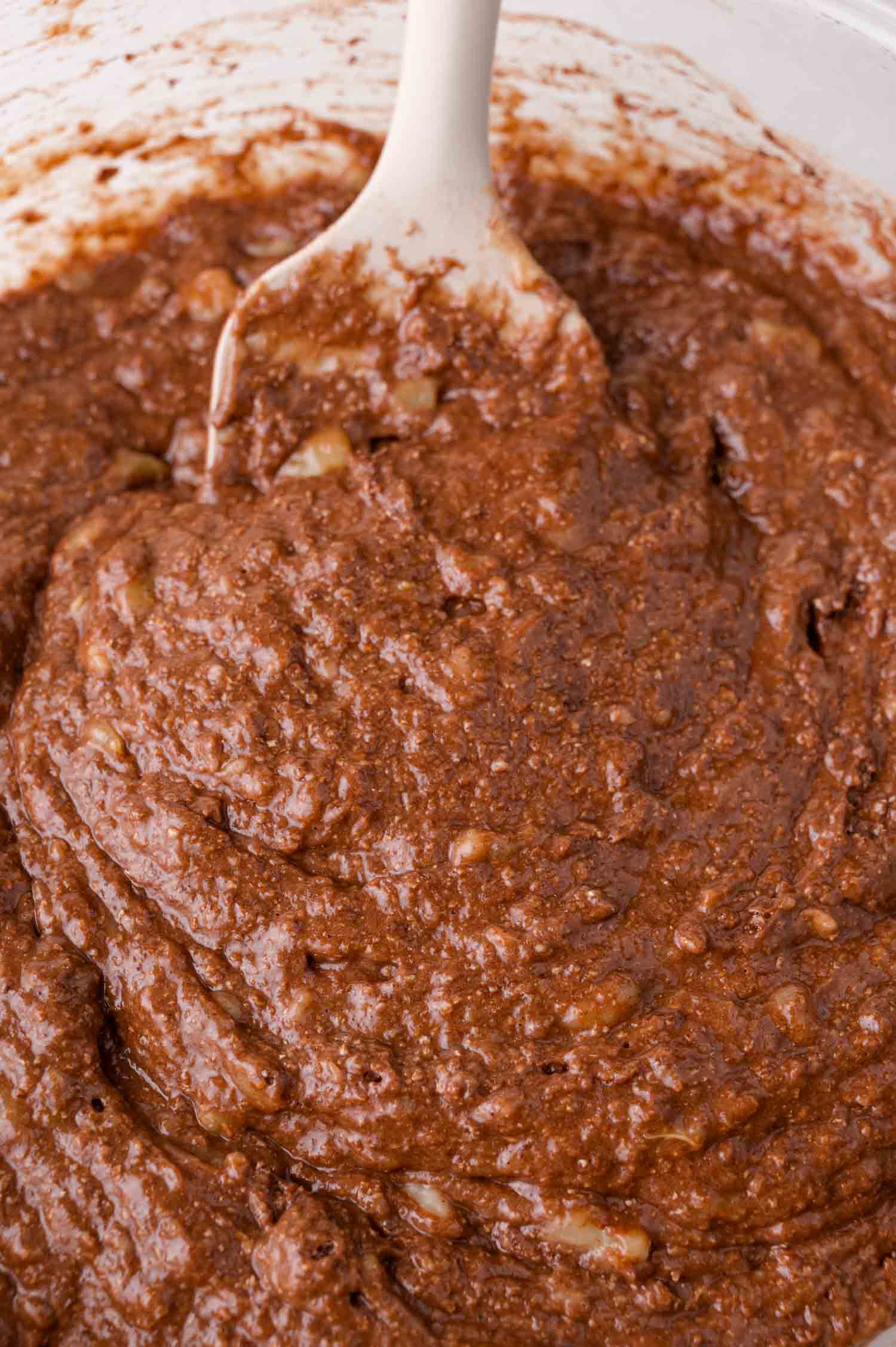 A close-up of a bowl filled with chocolate batter being mixed with a white spatula.