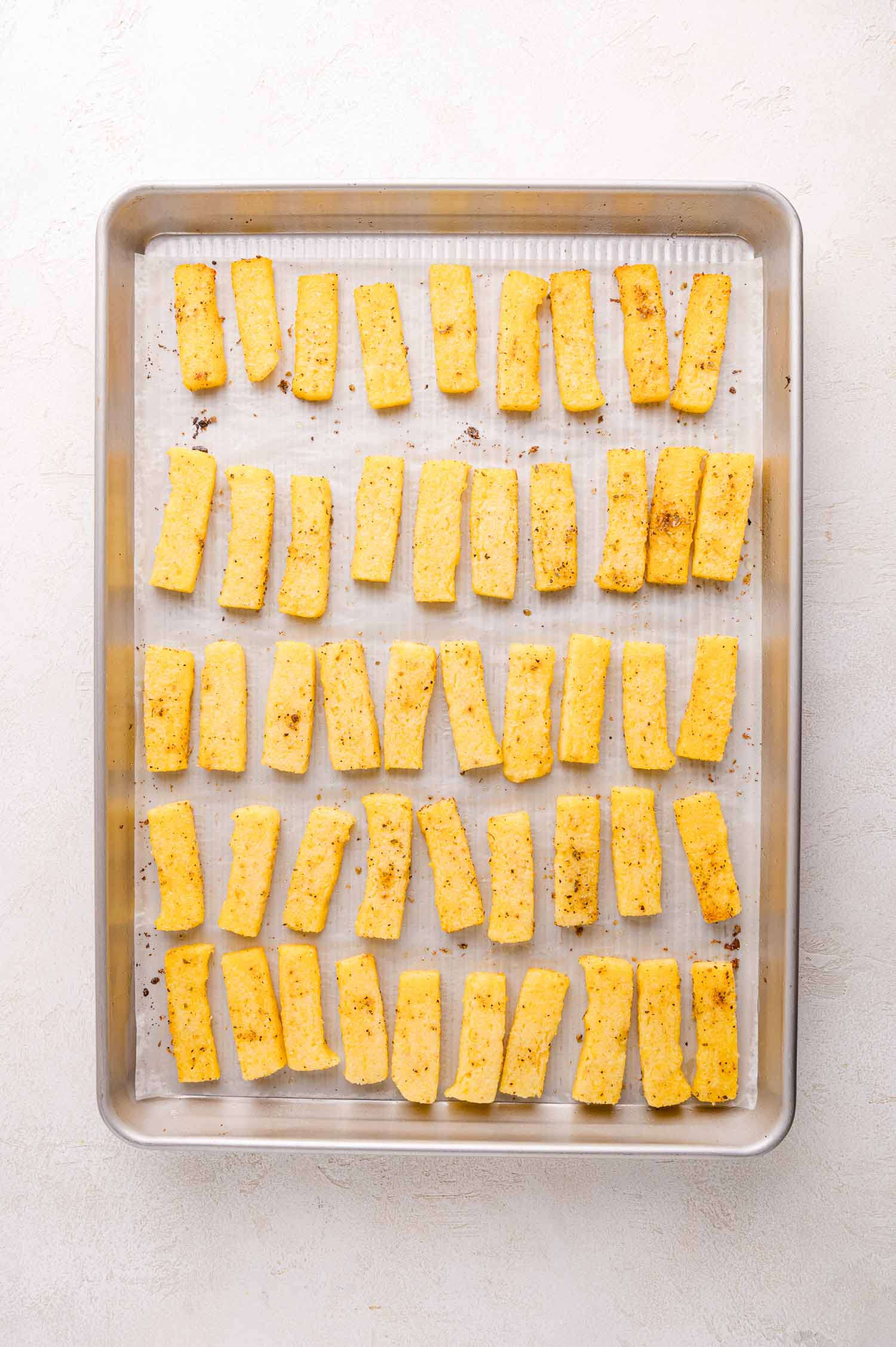 Rectangular pieces of seasoned polenta arranged in rows on a parchment-lined baking sheet.